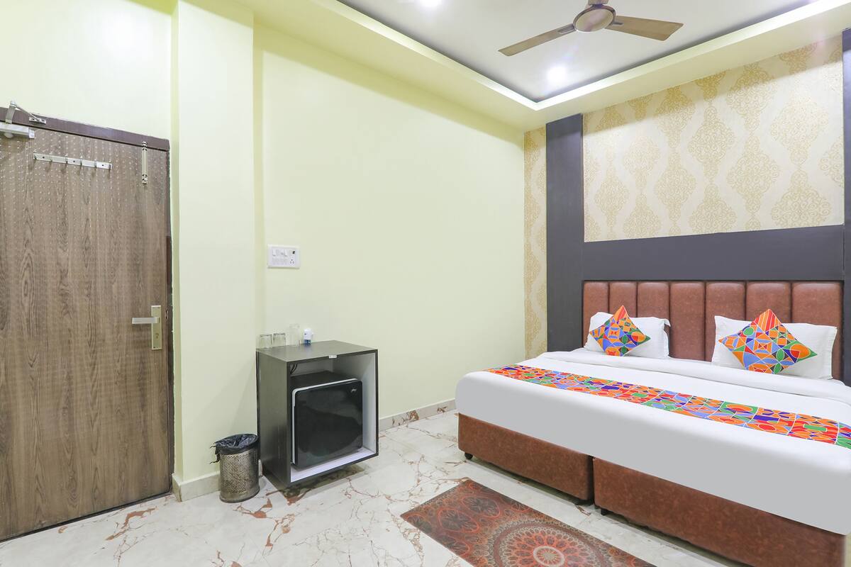 A bedroom with a bed, a ceiling fan, a small cabinet, and a trash bin.