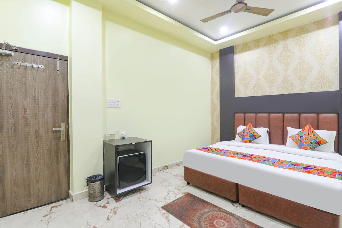 A bedroom with a bed, a ceiling fan, a small cabinet, and a trash bin.