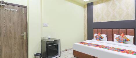 A bedroom with a bed, a ceiling fan, a small cabinet, and a trash bin.