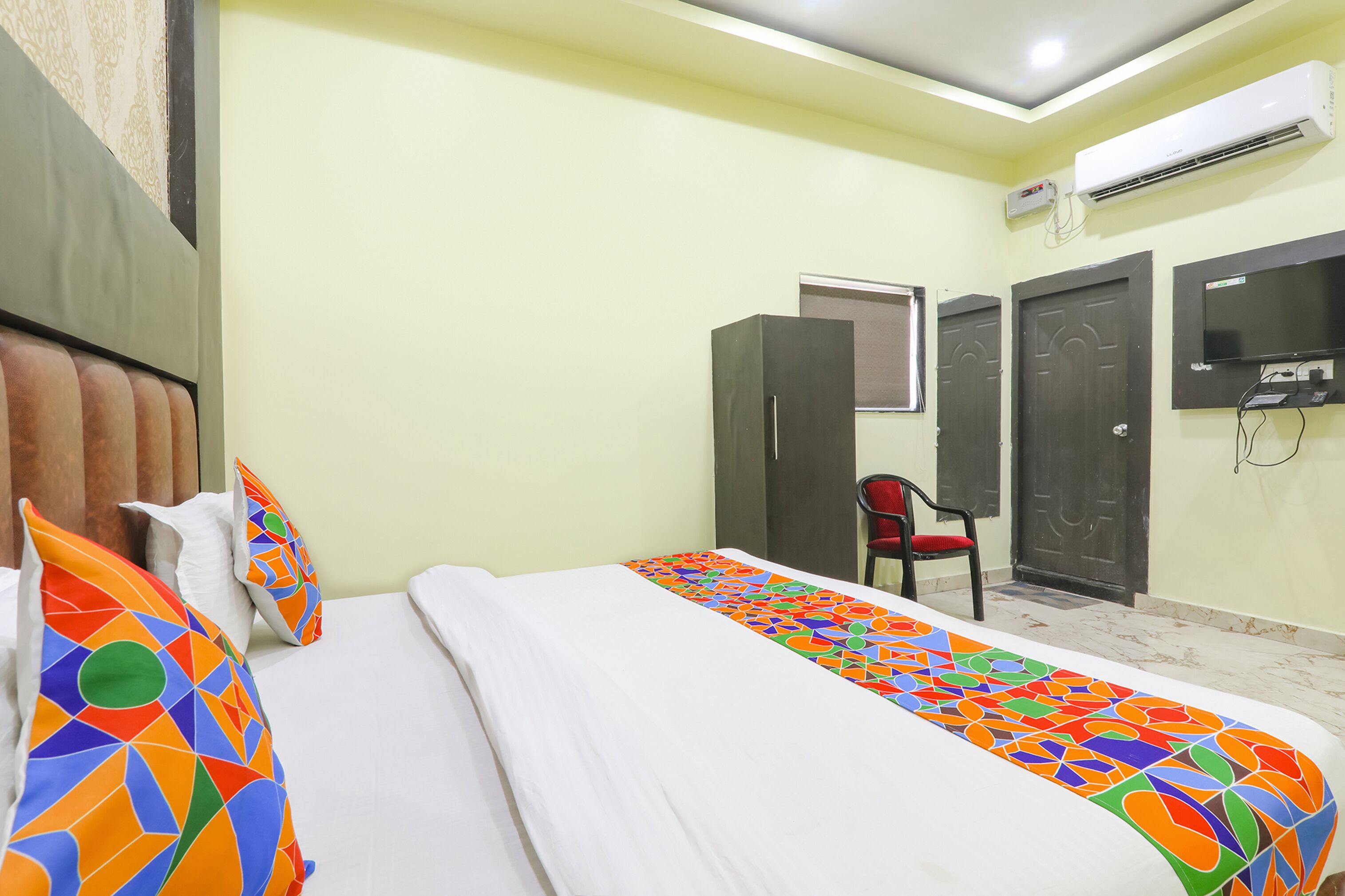 Une chambre d’hôtel équipée d’un lit, d’une chaise, d’un climatiseur et d’un téléviseur fixé au mur.