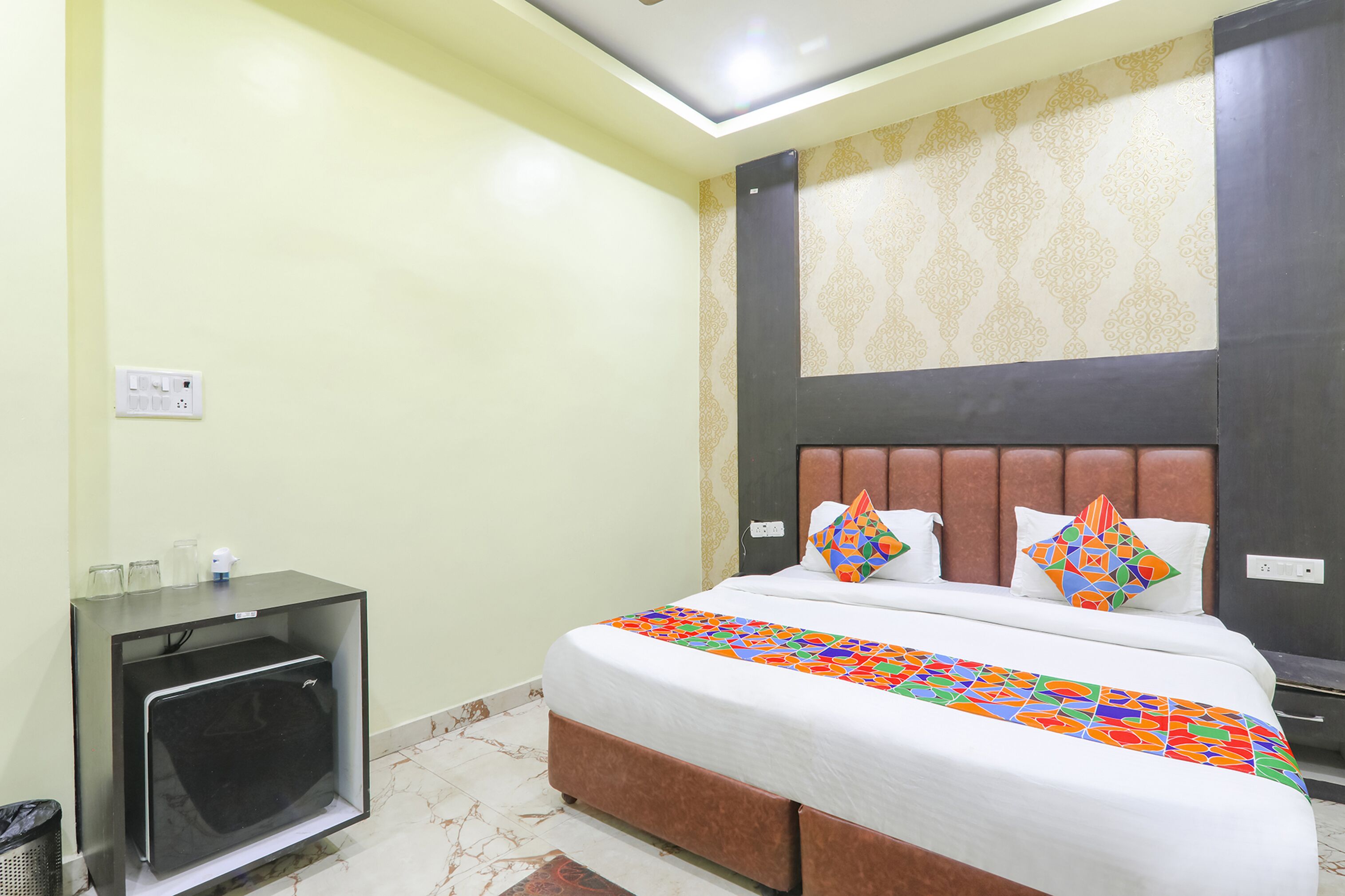 A hotel room with a bed, a small desk with a television, and a patterned wall.
