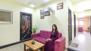 Zona de recepción con un sofá morado, una mesa de centro de madera y un ventilador.