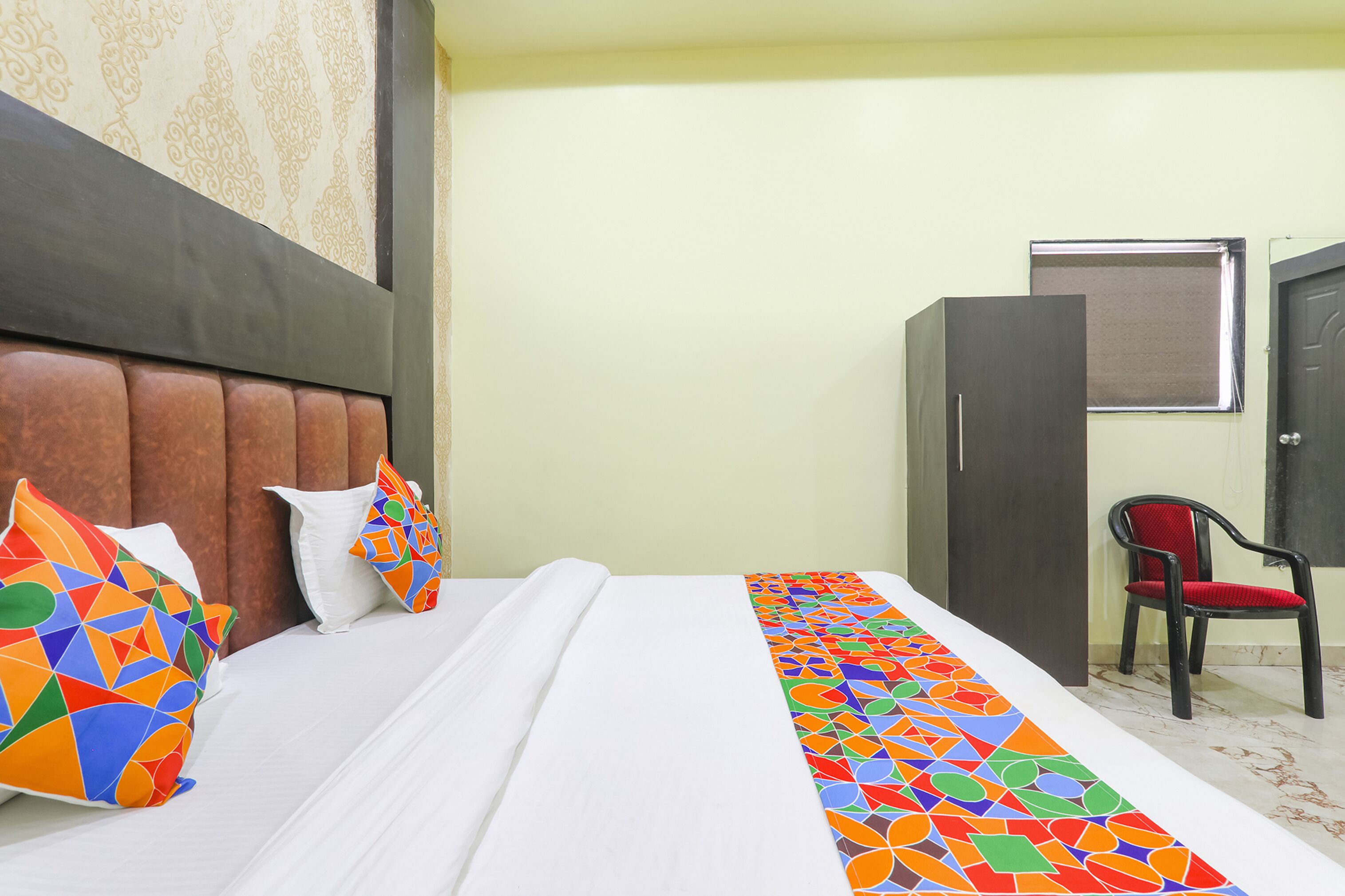 A hotel room with a bed, pillows, a chair, and a wardrobe.