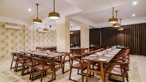Comedor con mesas y sillas de madera, iluminación colgante y papel tapiz estampado.