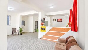 A hotel reception area with a check-in counter, a seating area with a sofa, and a staircase leading to an upper floor. - FabHotel Silver 9 (Paud)
