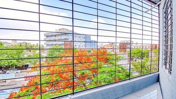 A view through a window with a metal grid, featuring a cityscape with buildings and trees. - FabHotel Silver 9 (Paud)