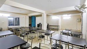 A hotel room with multiple tables and chairs, a large window, a curtain, and a ceiling fan.