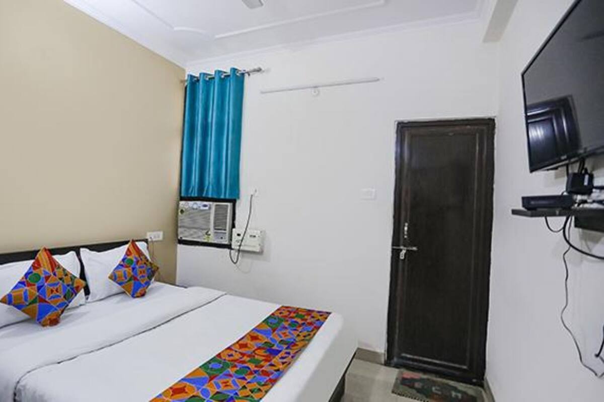 A hotel room with a bed, a television, a door, and a window with curtains.