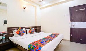 A hotel room with a large bed, a nightstand, a water bottle, a wall-mounted light, and a door. - Fabhotel Sai Govind (Rahata)