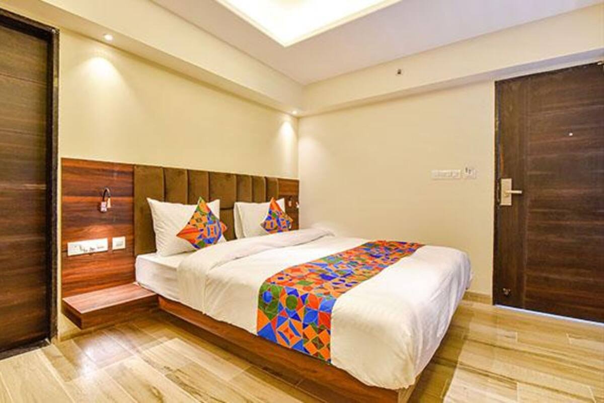 Un dormitorio con cabecera de madera, cama con ropa de cama blanca, almohadas coloridas y un plaid estampado geométrico.