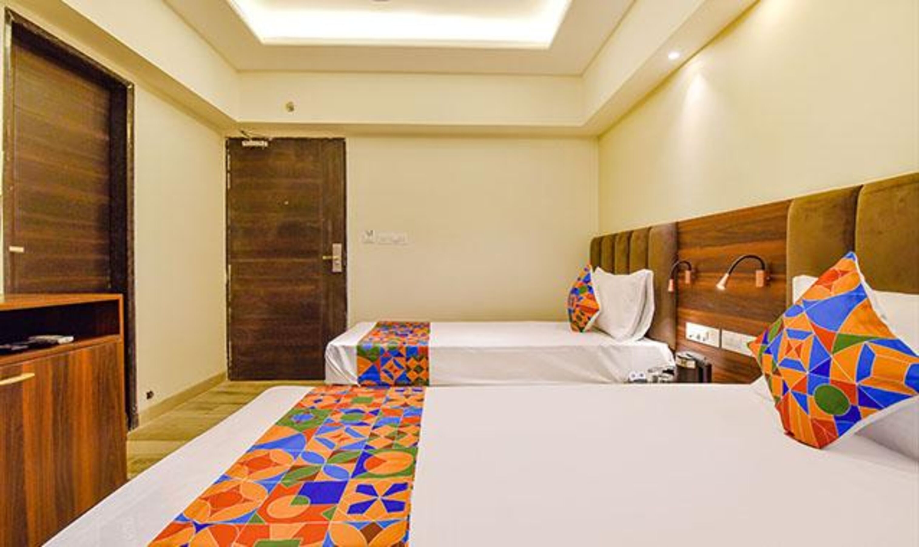 A hotel room with two beds, a wooden wardrobe, and a door.