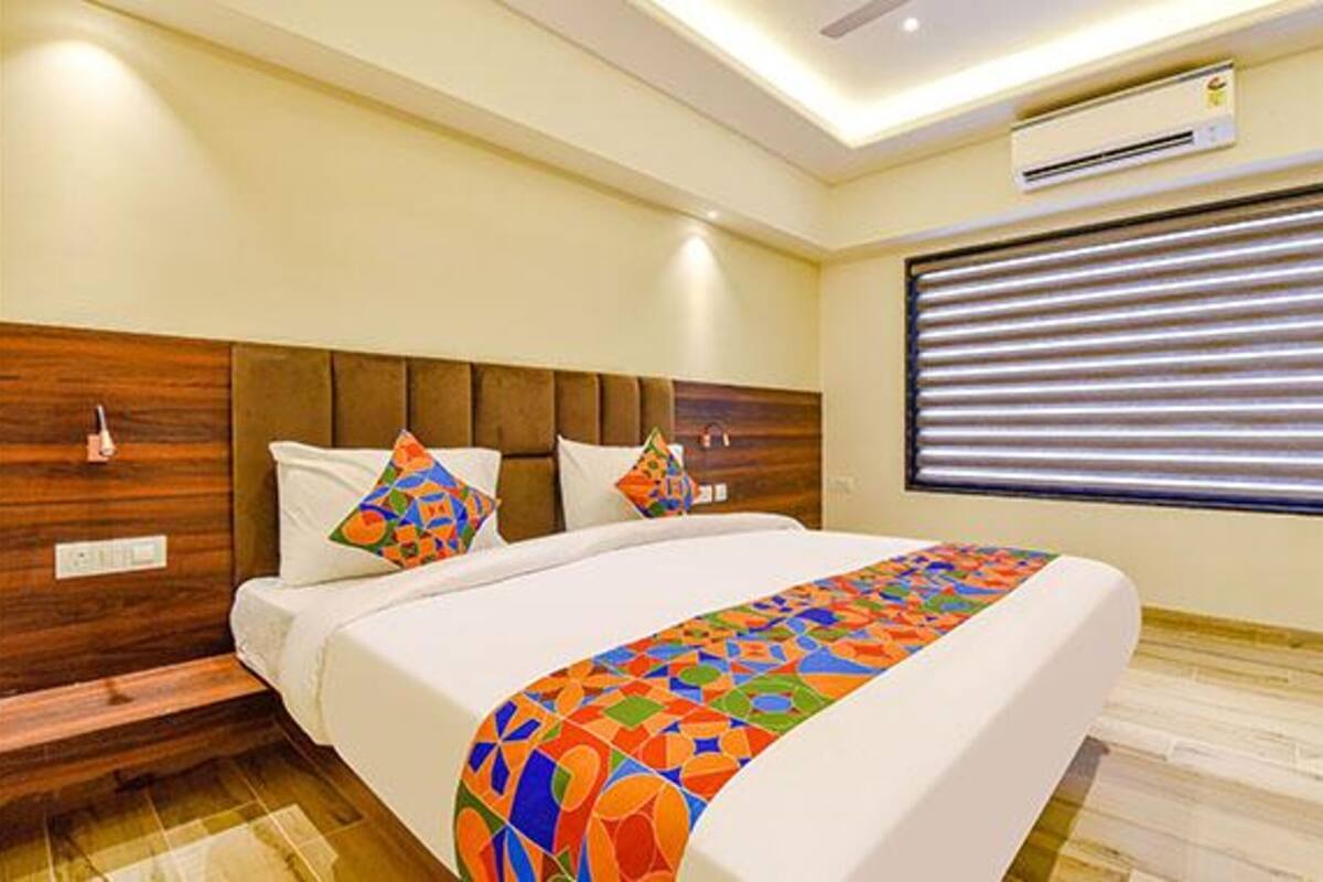 Una habitación de hotel moderna con cabecera de madera, una cama grande con ropa de cama colorida, una ventana con persianas y un equipo de aire acondicionado en la pared.