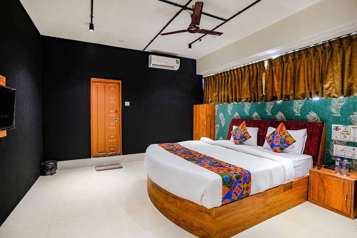 A bedroom with a bed, a wooden wardrobe, a ceiling fan, an air conditioning unit, and a window with curtains.