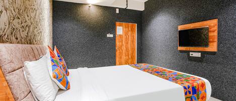Un dormitorio moderno con cama, cabecera de madera, ventilador de techo, televisor montado y una puerta con panel de madera.