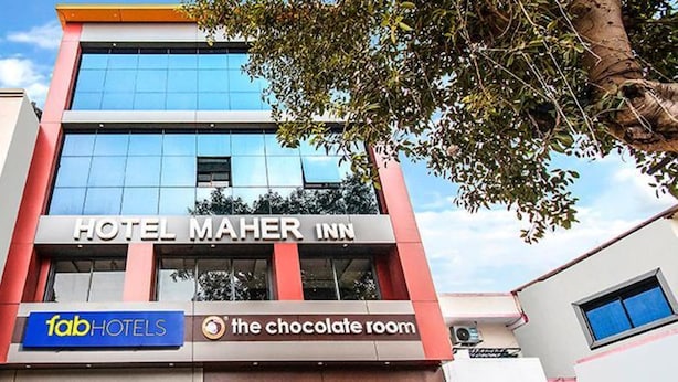 Um hotel chamado Hotel Maher Inn com fachada moderna, incluindo uma janela de vidro e uma placa com 'fabHOTELS' e 'the chocolate room'.
