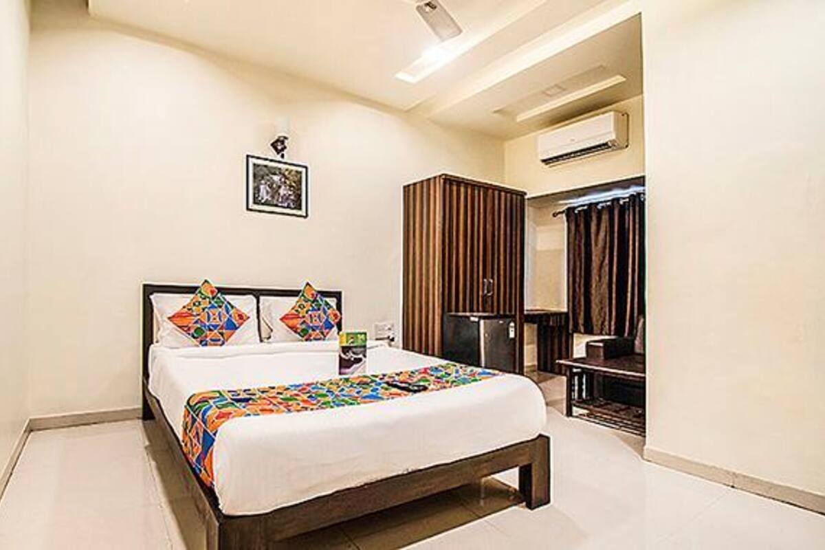 A hotel room with a bed, a wardrobe, a mirror, and an air conditioning unit.