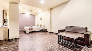 Um quarto espaçoso com uma cama grande, um sofá marrom e uma mesa pequena.