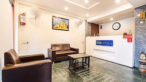 Uma área de recepção de hotel com balcão, um relógio, um extintor de incêndio e um quadro na parede.