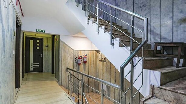 A staircase with metal railings, a wooden wall, and a fire extinguisher mounted on the wall. - Fabexpress Station Ii (New Delhi)