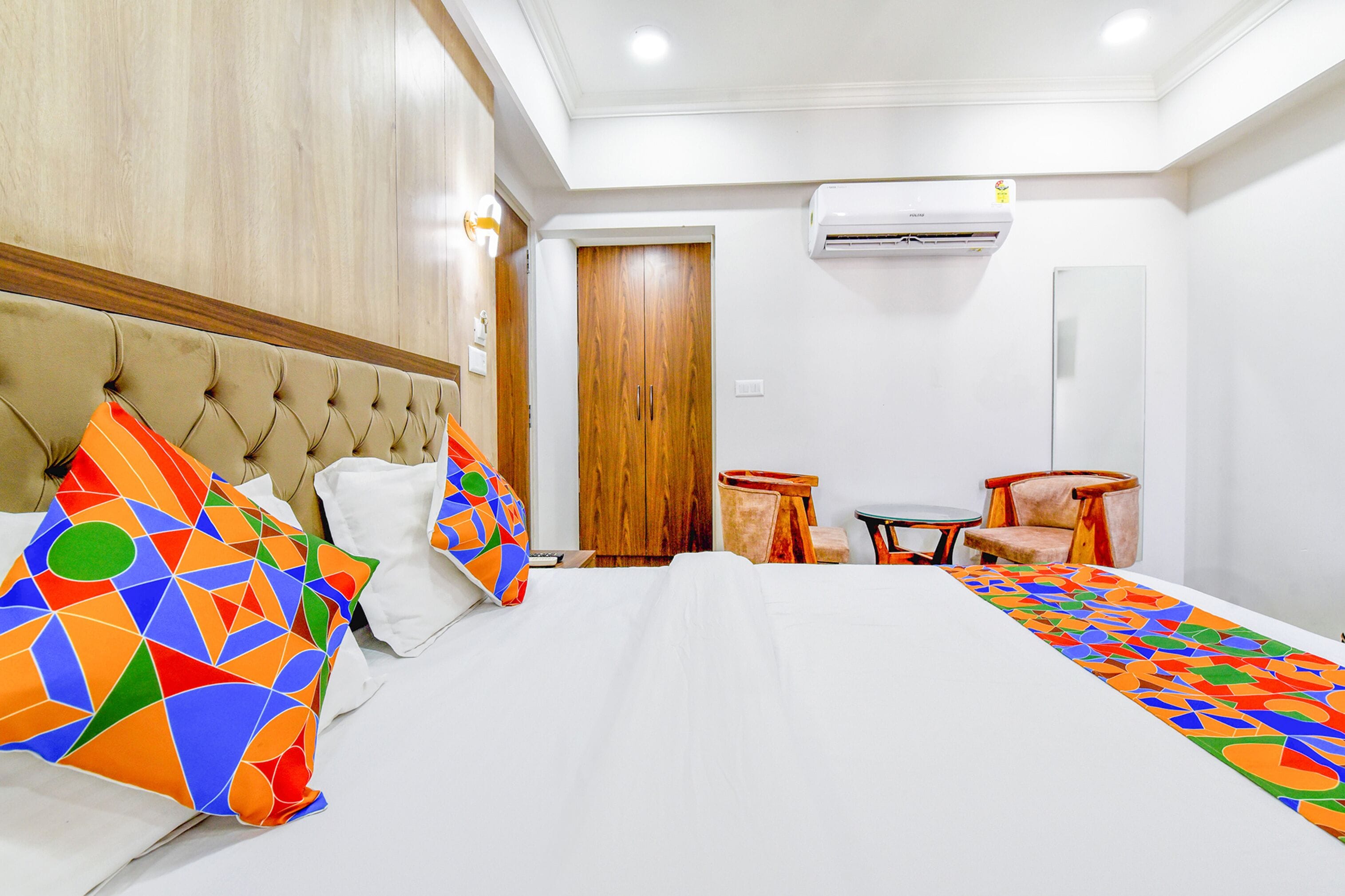 A hotel room with a large bed, a wooden wardrobe, a small round table, and a chair.