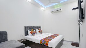 A modern hotel room with a bed, a grey sofa, a TV mounted on the wall, and an air conditioning unit. - Fabexpress Bhau Residency (Mumbai)