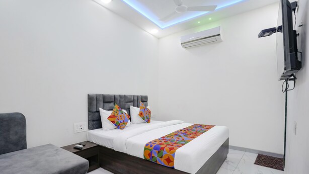 A modern hotel room with a bed, a grey sofa, a TV mounted on the wall, and an air conditioning unit. - Fabexpress Bhau Residency (Mumbai)