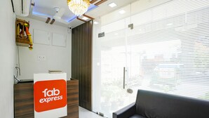 A reception area with a 'fab express' sign, a wooden reception desk, a black sofa, and a large window with blinds. - Fabexpress Bhau Residency (Mumbai)