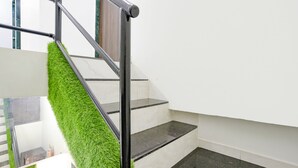 A staircase with a green artificial grass wall, black handrails, and white walls. - Fabexpress Bhau Residency (Mumbai)