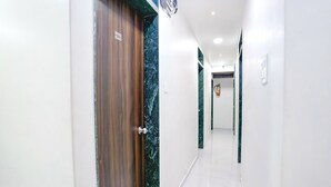 A hallway with a wooden door, white walls, and a marble accent wall. - Fabexpress Bhau Residency (Mumbai)