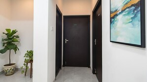 Un couloir avec une porte sombre, une plante en pot et un tableau abstrait encadré accroché au mur.