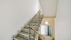 Un escalier avec des marches en marbre et des rampes en métal, menant à un palier doté d’une fenêtre avec des stores.