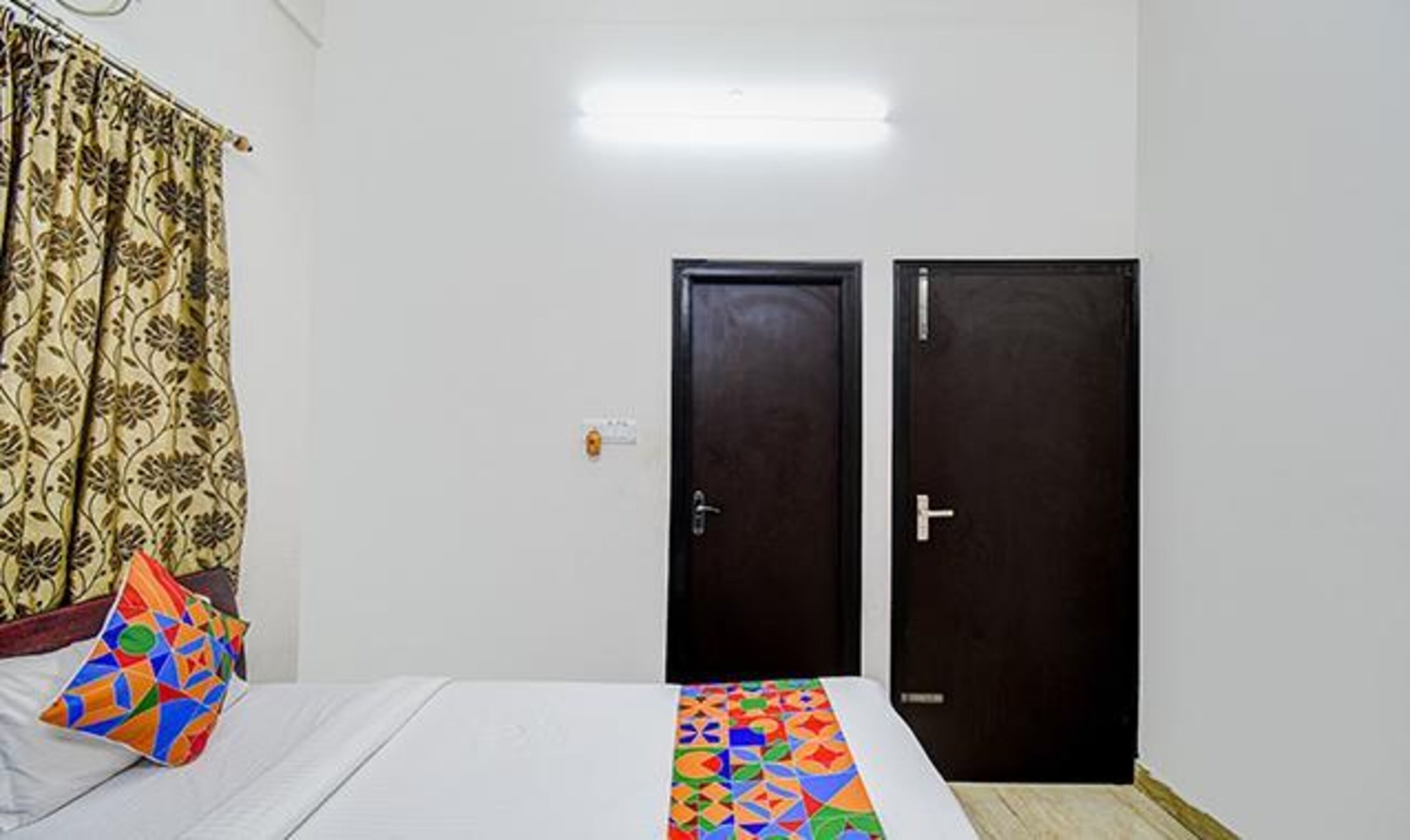Une chambre à coucher avec un lit, un coussin coloré, un rideau à motifs et deux portes sombres.