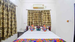 Une chambre d’hôtel avec un lit, des rideaux, un climatiseur et une couvre-lit aux couleurs vives.