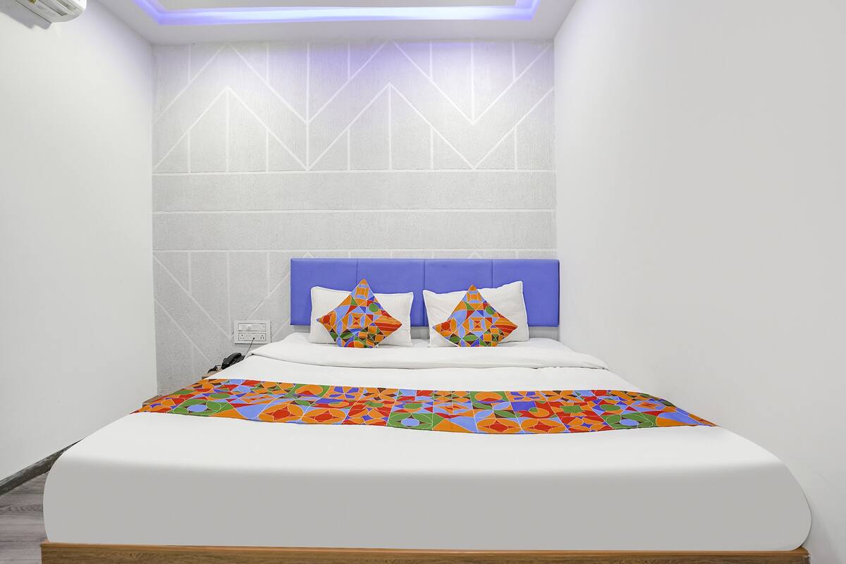 Un dormitorio moderno con una cama blanca, cabecera azul y almohadas de colores con motivos geométricos.