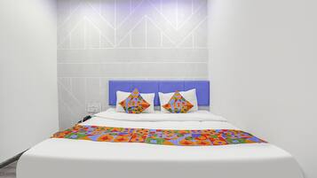 Un dormitorio moderno con una cama blanca, cabecera azul y almohadas de colores con motivos geométricos.