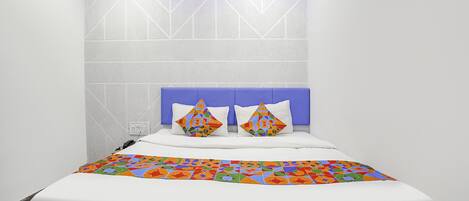 Un dormitorio moderno con una cama blanca, cabecera azul y almohadas de colores con motivos geométricos.