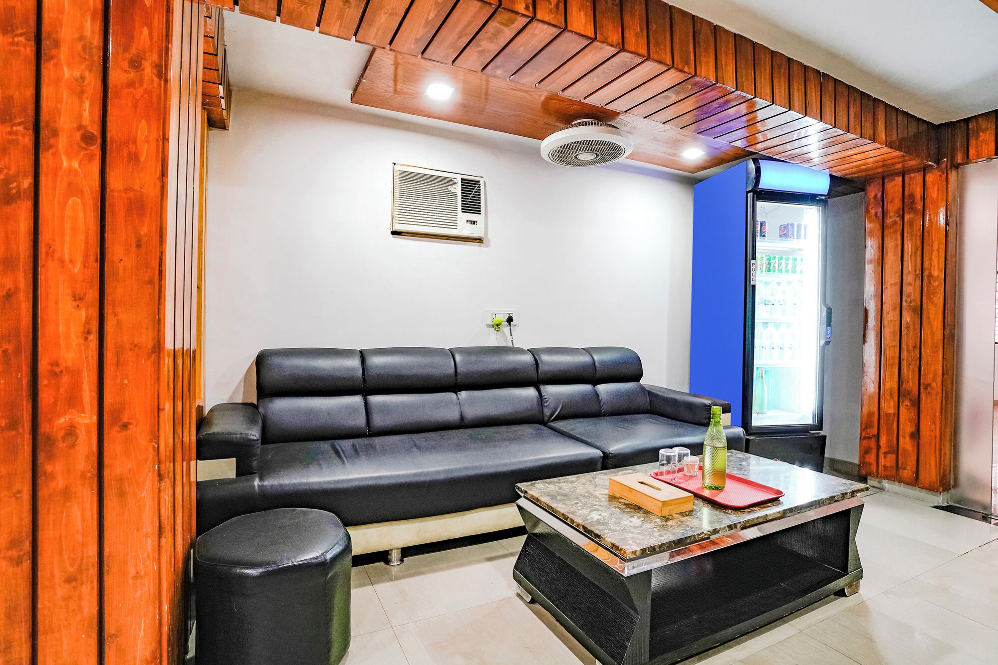A modern living room with a black leather sofa, a marble coffee table, and a built-in air conditioning unit.