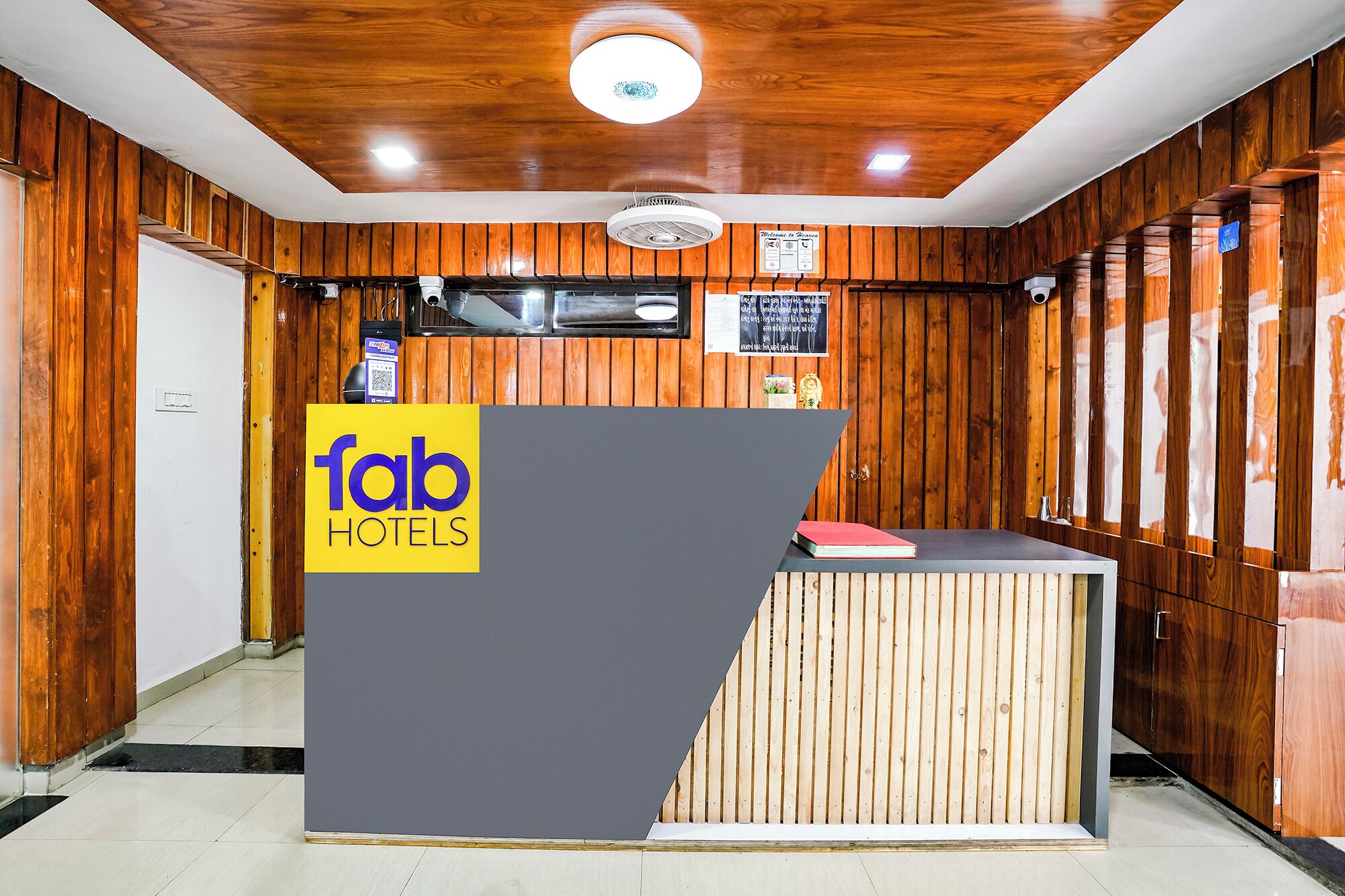 Een receptiebalie met een 'fab hotels' bord, houten lambrisering, een plafondventilator en een kleine klok.