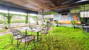 Un área de comedor al aire libre con mesas y sillas, un mural en la pared y un césped.