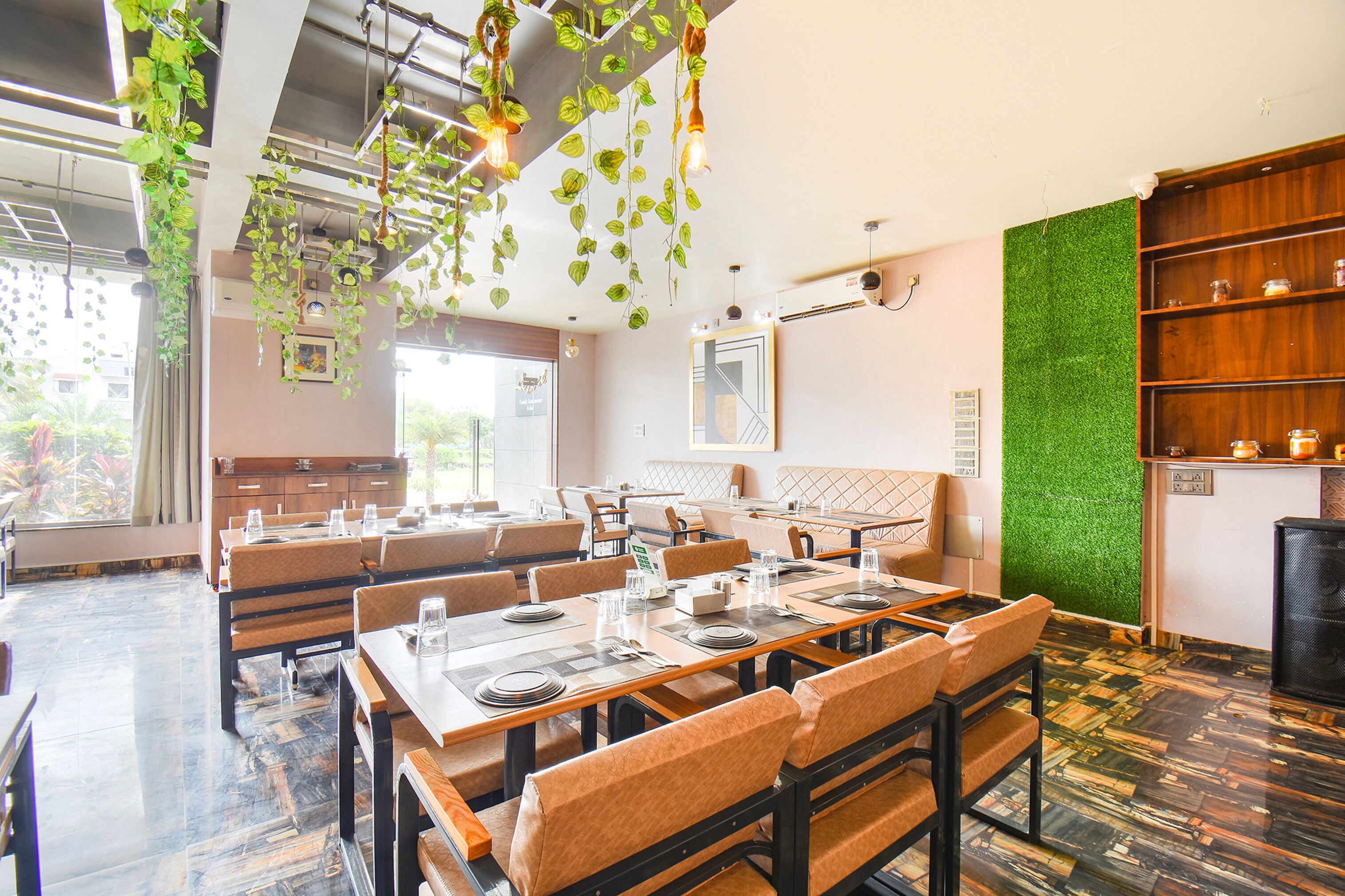 A restaurant with multiple tables and booths, hanging plants, and a green wall.