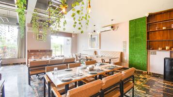 A restaurant with multiple tables and booths, hanging plants, and a green wall.