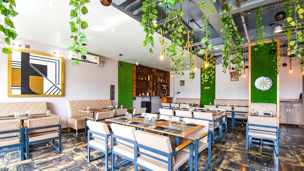 Un restaurante con cabinas y mesas, paredes verdes y plantas colgantes.