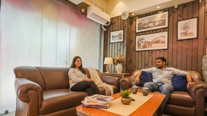A living room with two brown leather sofas, a wooden coffee table, and framed pictures on the wall. - Fabhotel Naman (Kanpur)