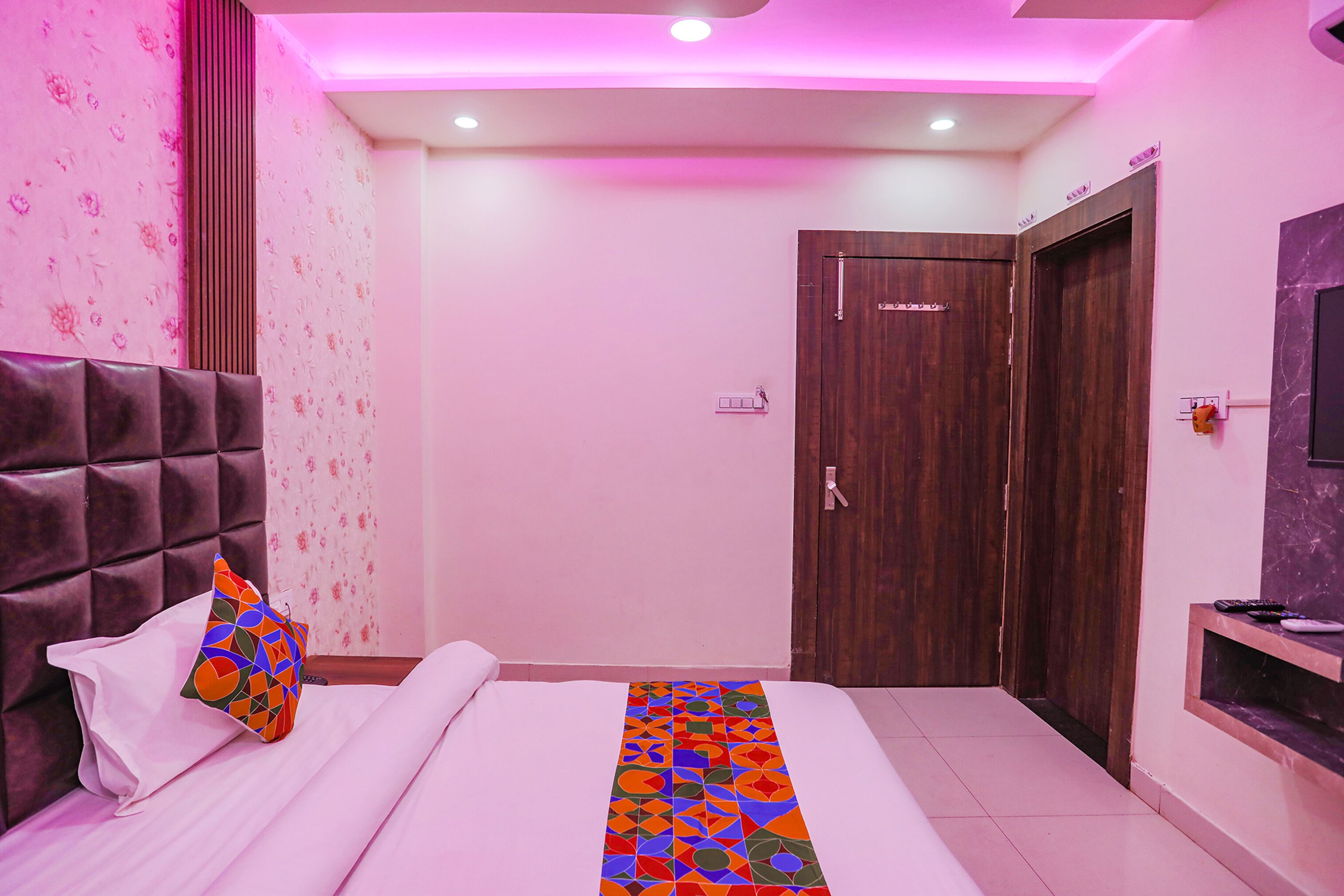 Una habitación de hotel con cama, cabecera, puerta de madera y televisor en la pared.