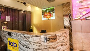 A hotel reception area with a marble reception desk, a ceiling fan, and a television screen displaying a decorative image. - Fabhotel Naman (Kanpur)