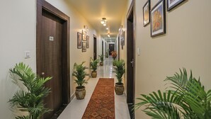 A hotel hallway with wooden doors, potted plants, framed artwork, and a patterned carpet. - Fabhotel Naman (Kanpur)