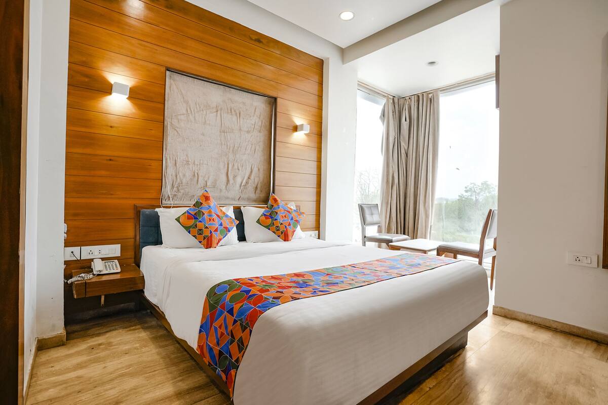 A hotel room with a large bed, wooden headboard, two bedside tables, a telephone, and a window with curtains.