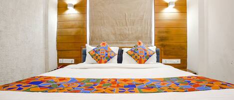 Hotelkamer met een houten hoofdbord, twee wandlampen, een groot raam en een kleurrijke deken met een geometrisch patroon.