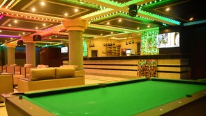Une table de billard dans une pièce comprenant un bar, des sièges confortables et un mur décoré de motifs.
