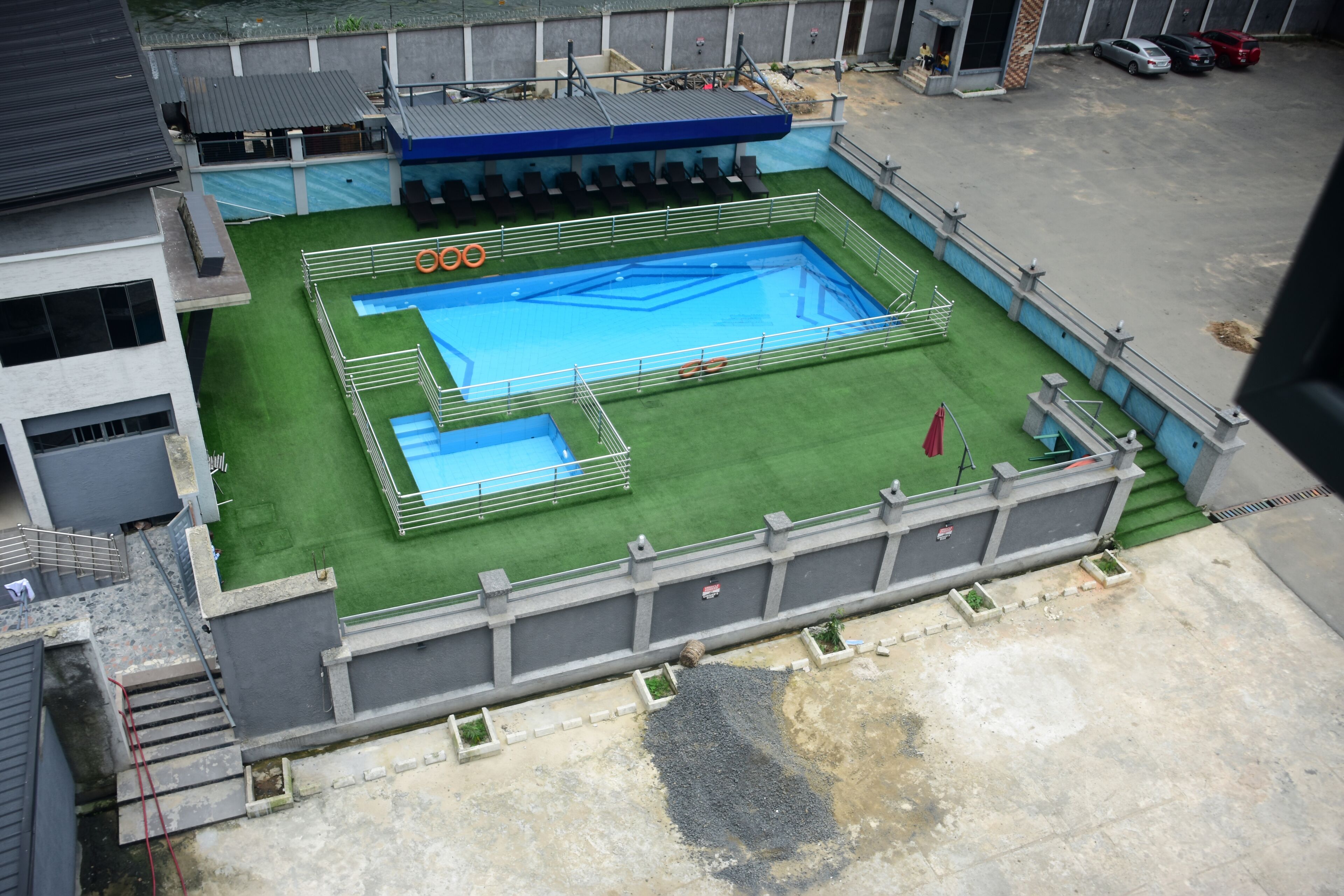 A rooftop swimming pool with a blue water feature, surrounded by a green lawn and a concrete deck.